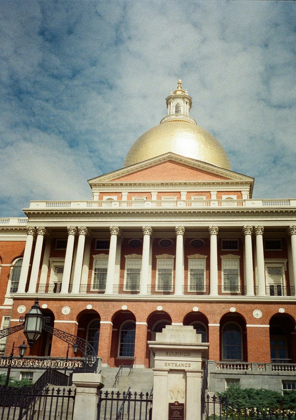 The gold dome of the Massachusetts State House against a cloudy blue sky