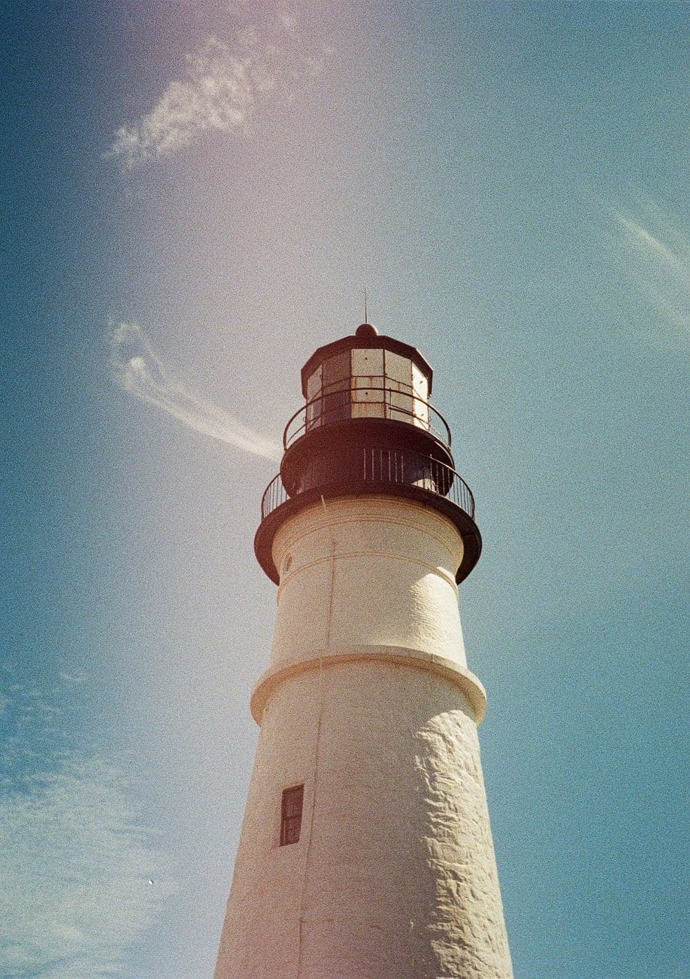 A white lighthouse shot from below against a blue sky, with a soft light leak across the frame