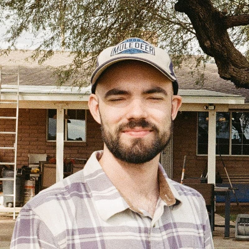 Hayden Harrison outdoors in a plaid shirt and cap, smiling