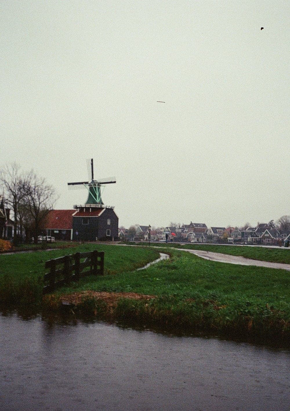 A green windmill above wet fields and a canal on an overcast day